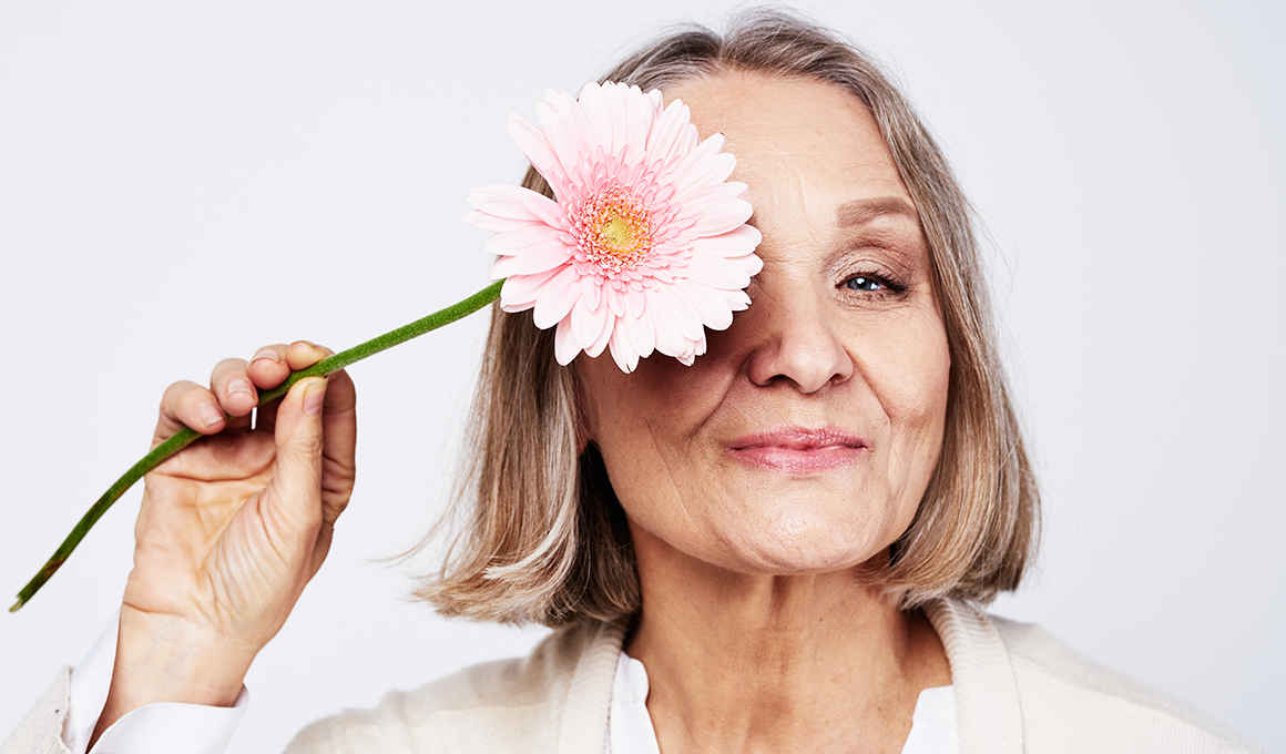 Mujer de edad avanzada que sujeta una flor. La foto representa la menopausia.